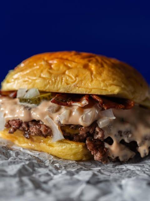 Smash burger d'Alpa amb cheddar fos i bacon sobre fons blau